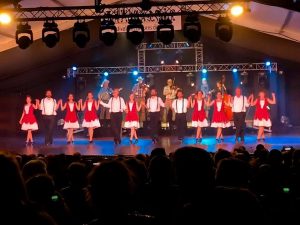 Wild Goose Chase Cloggers on stage, gents in white and black and ladies in red dresses
